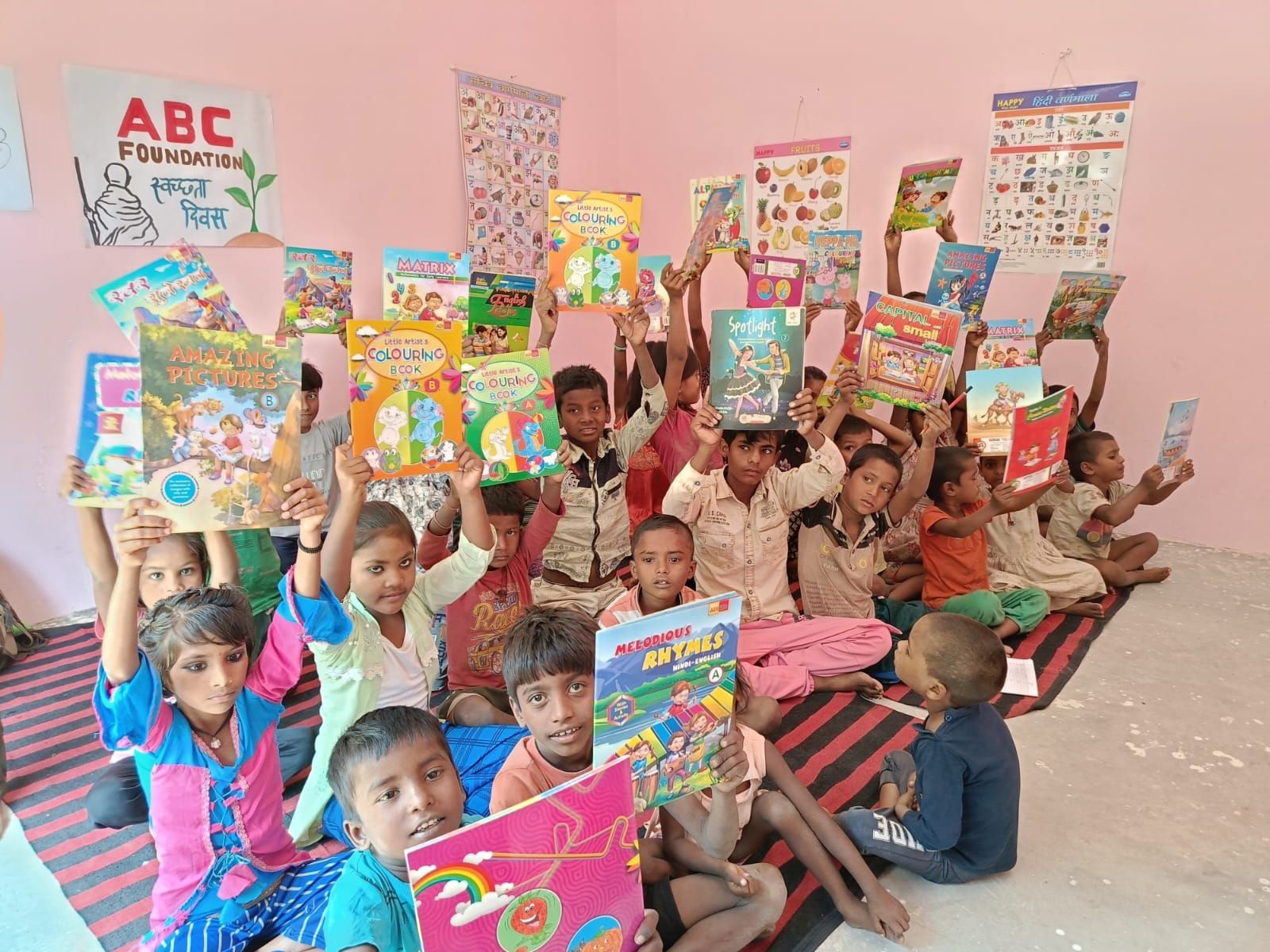 Group of children in a classroom holding colorful books, with educational posters on the walls.