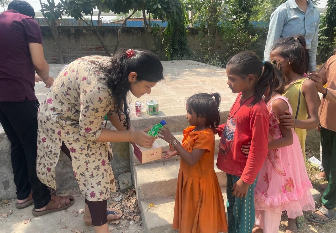 Woman giving drinks to children outdoors, surrounded by greenery.